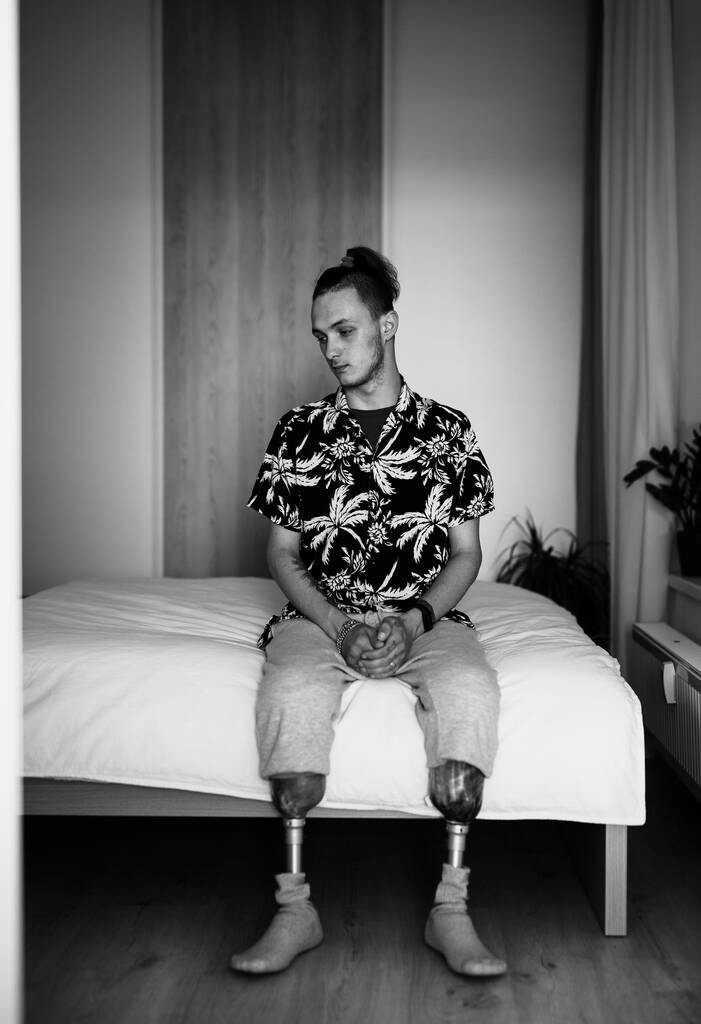 Retrato preto e branco do jovem deficiente sentado na cama em casa, conceito de prótese de perna. - Foto, Imagem