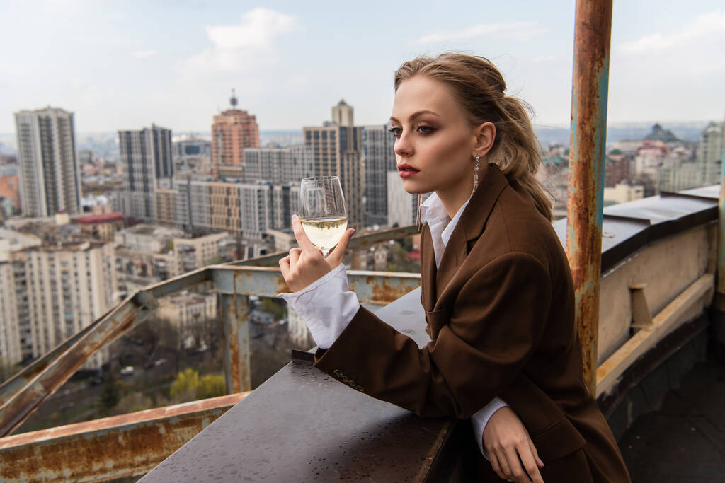 молода жінка тримає келих білого вина на даху з міським пейзажем на розмитому фоні
 - Фото, зображення