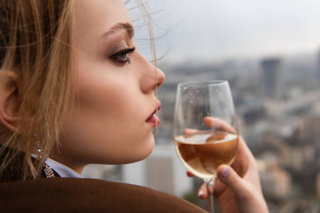 κοντινό πλάνο της όμορφης γυναίκας κρατώντας ένα ποτήρι κρασί με το αστικό τοπίο σε θολή φόντο - Φωτογραφία, εικόνα