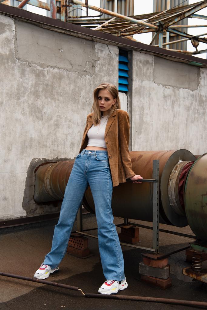 full length of blonde woman in jeans, suede blazer and trendy sneakers posing on rooftop - Photo, Image