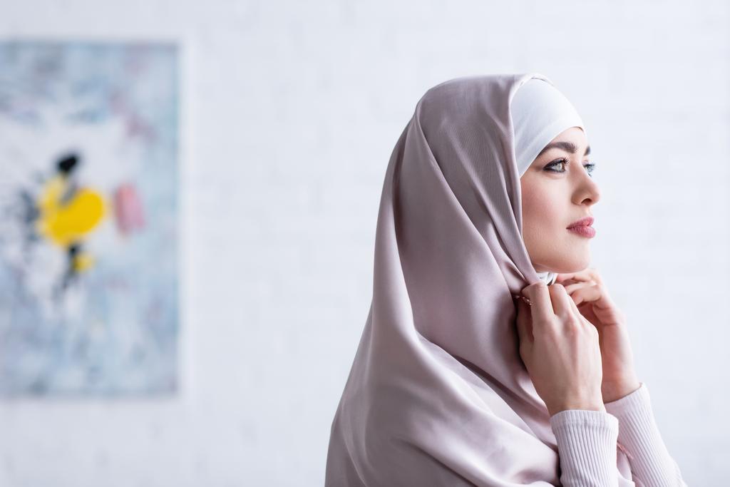 giovane donna musulmana guardando lontano mentre regola hijab a casa - Foto, immagini
