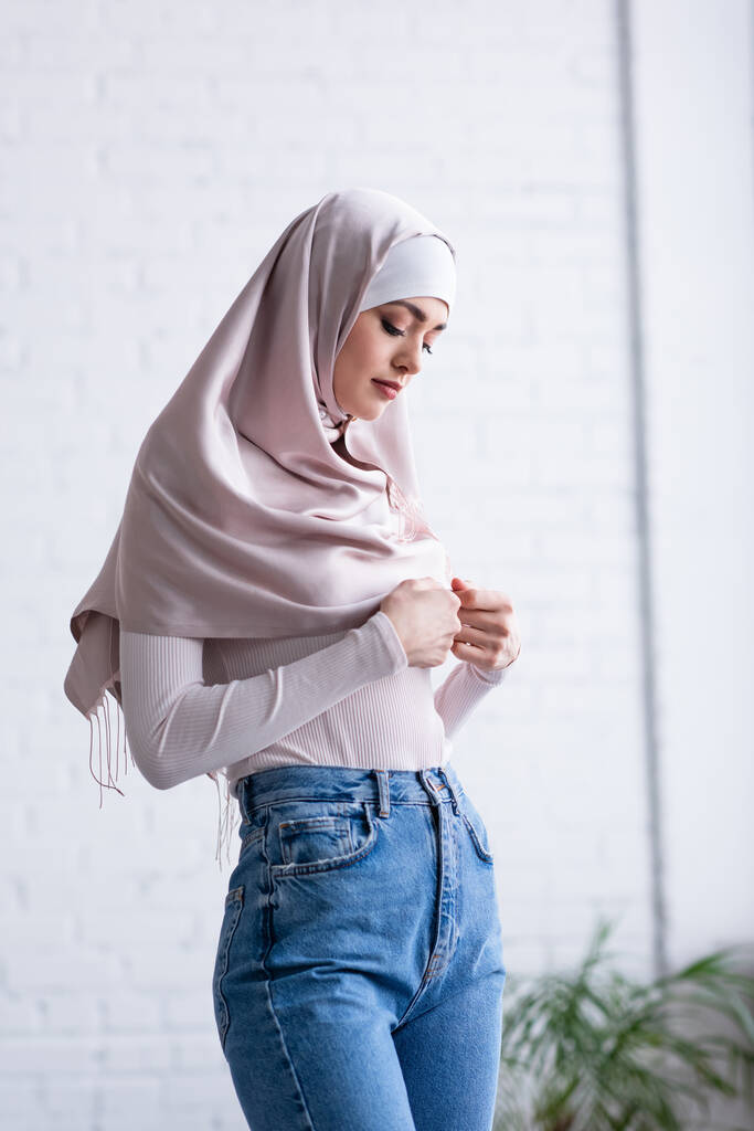 tímida mujer musulmana tocando hijab mientras está de pie en casa - Foto, imagen