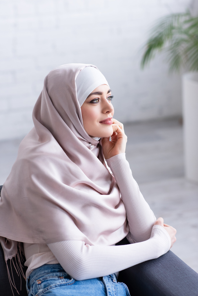 sognante donna musulmana sorridente mentre distoglie lo sguardo da casa - Foto, immagini