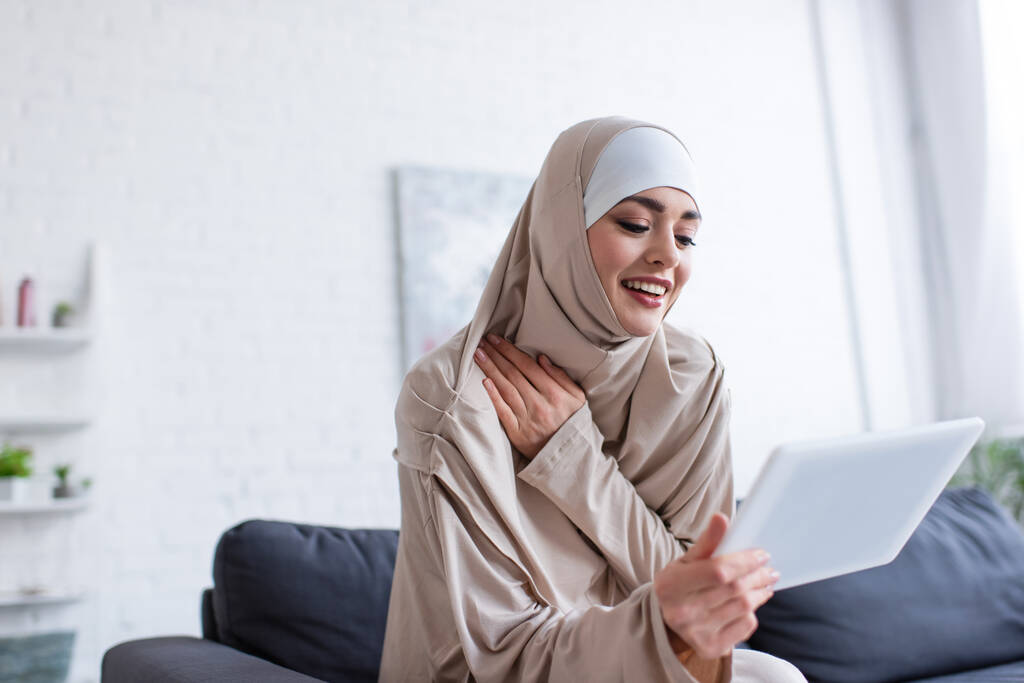 wesoła arabska kobieta w hidżabie korzystająca z tabletu cyfrowego w domu - Zdjęcie, obraz
