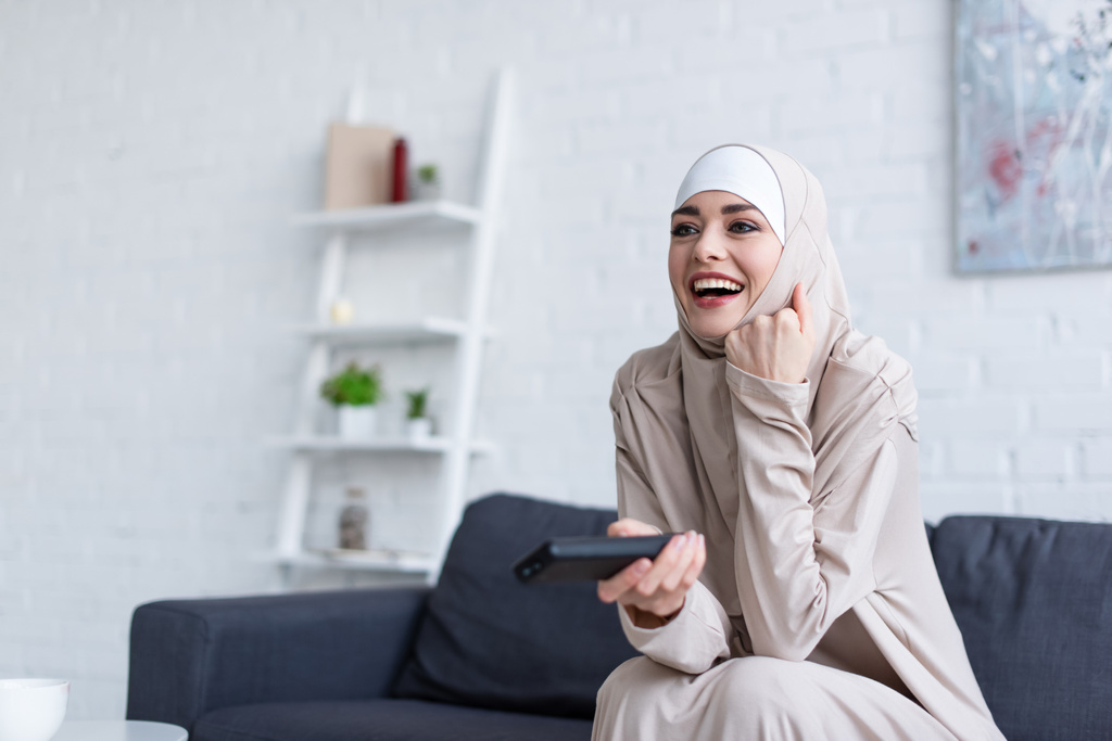 aufgeregte arabische Frau lacht, während sie sich zu Hause einen Film ansieht - Foto, Bild