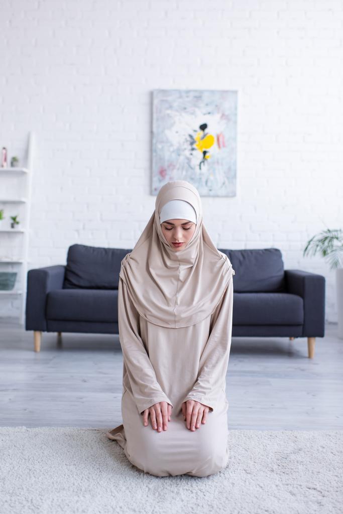 молода мусульманка молиться, сидячи на підлозі з закритими очима
 - Фото, зображення