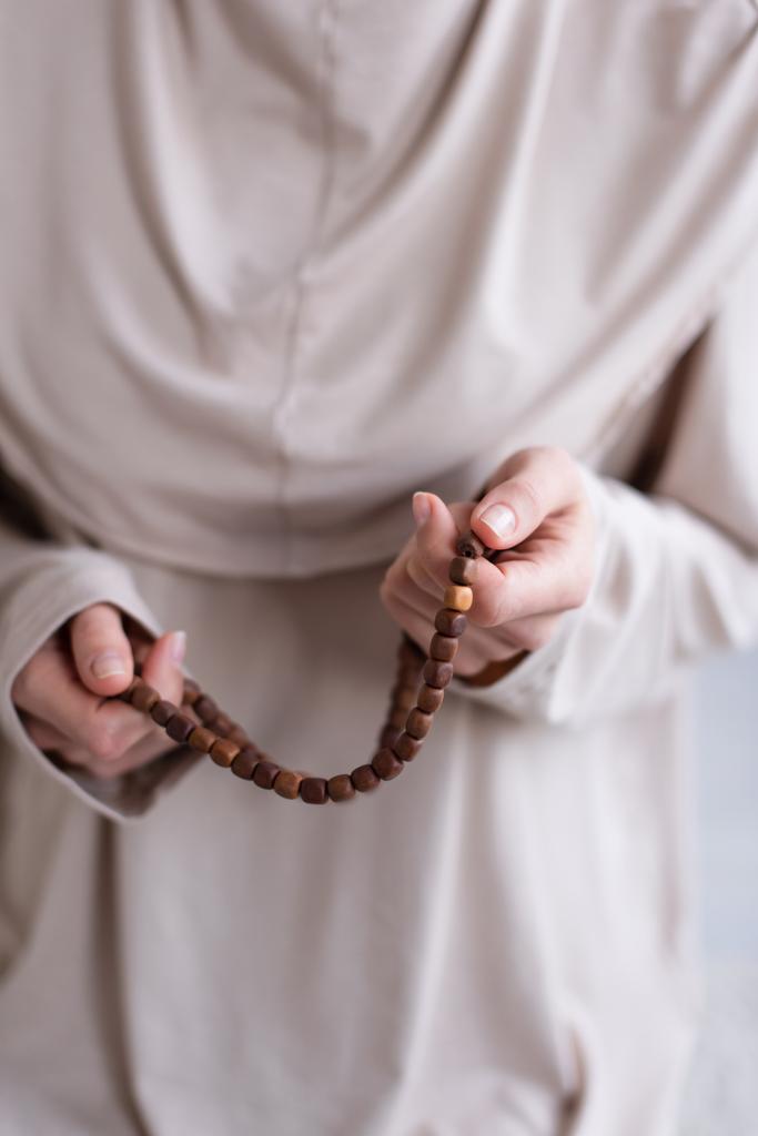 enfoque selectivo del rosario en las manos de la mujer musulmana borrosa rezando en casa, vista recortada - Foto, imagen