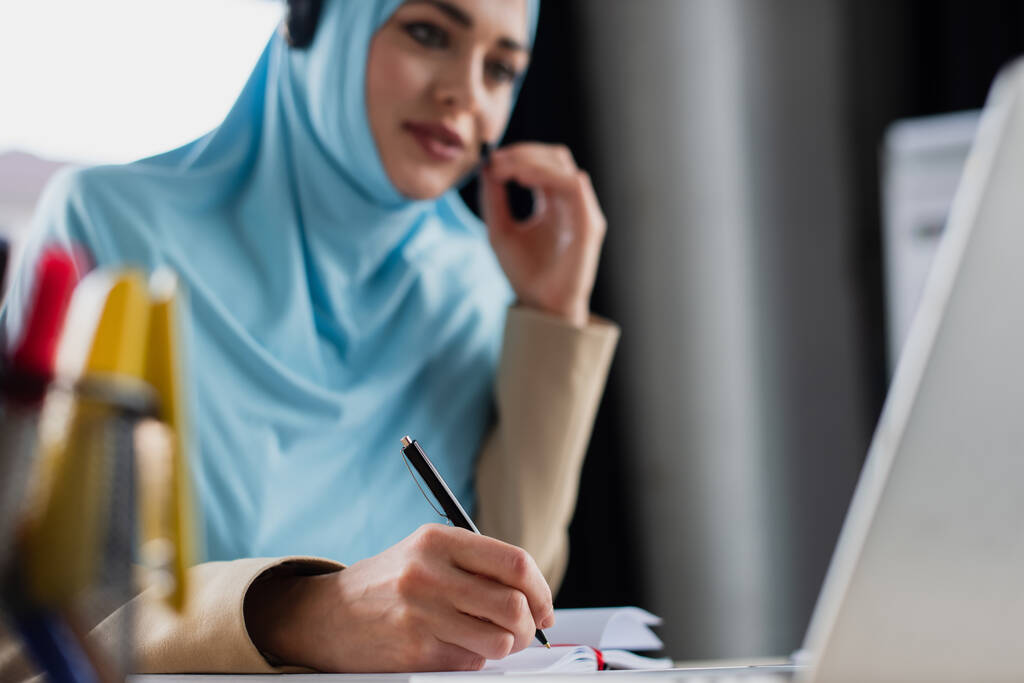 blurred muslim woman writing in notebook while working in call center - Photo, Image