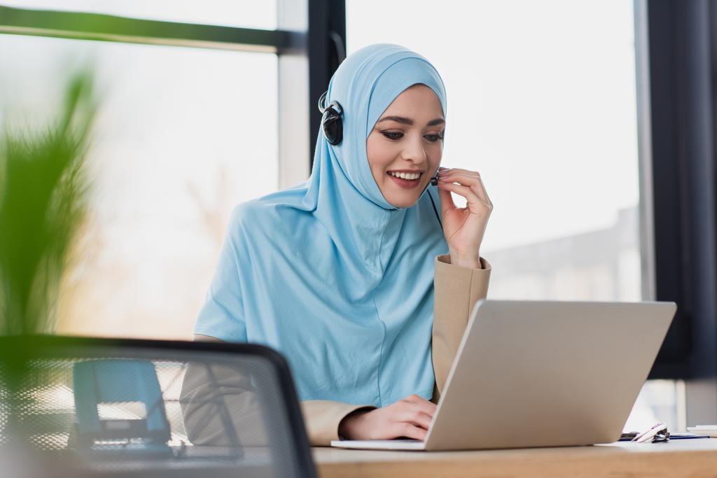 donna musulmana sorridente che usa il computer portatile mentre lavora nel call center - Foto, immagini