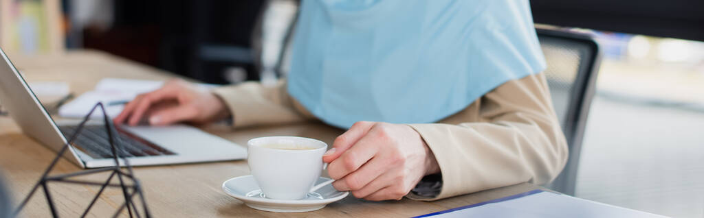 vista recortada de la mujer de negocios musulmana cerca de la computadora portátil y taza de café en la oficina, pancarta - Foto, Imagen