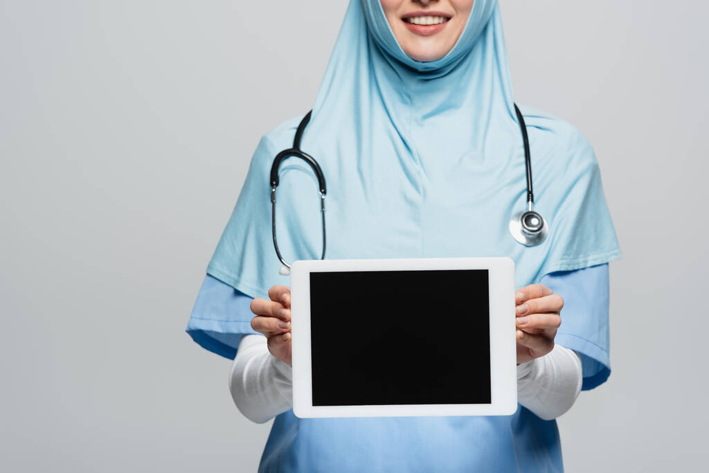 rajattu näkymä hymyilevä muslimi lääkäri näyttää digitaalinen tabletti tyhjä näyttö eristetty harmaa - Valokuva, kuva