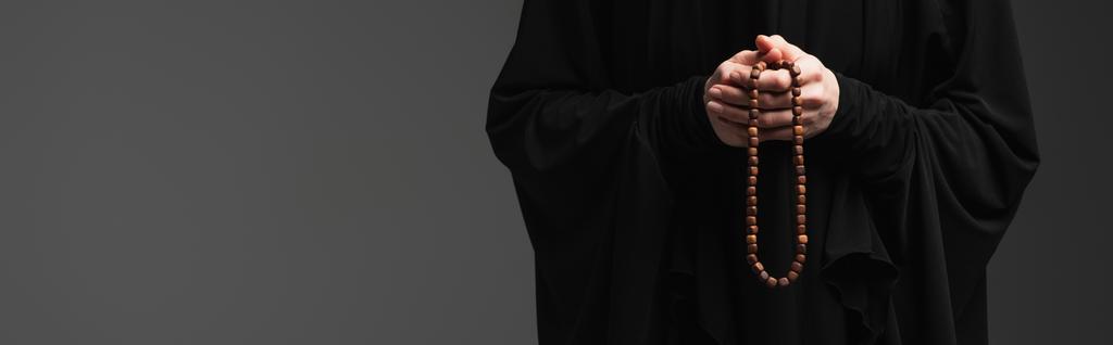 przycięty widok na muzułmańską zakonnicę z różańcem modlącą się odizolowany na ciemnoszarym, sztandar - Zdjęcie, obraz