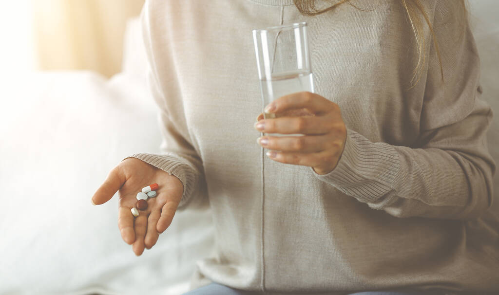 Close-up-Frau hält Tabletten Zeit, um Medikamente zu nehmen, Heilmittel für Kopfschmerzen. Medizinkonzept während der Selbstisolation und Coronavirus-Pandemie - Foto, Bild