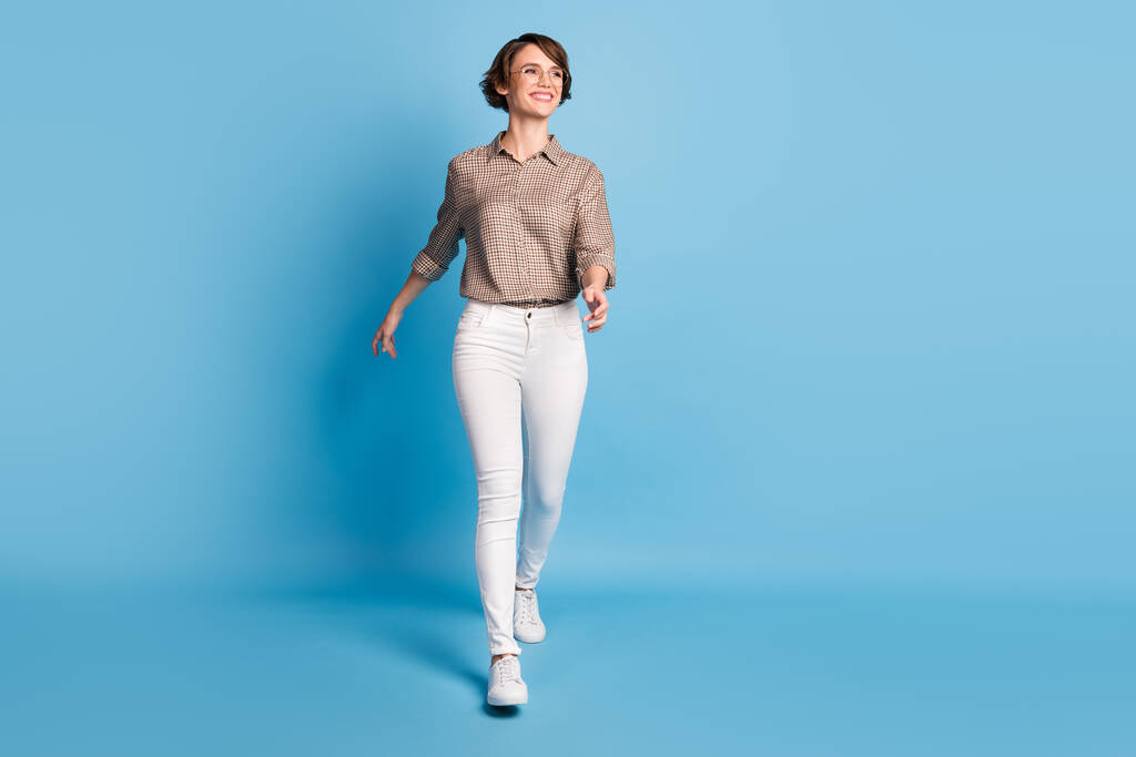 Full-Size-Porträt von selbstbewussten fröhlichen Dame zu Fuß aussehen leeren Raum strahlendes Lächeln isoliert auf blauem Hintergrund - Foto, Bild