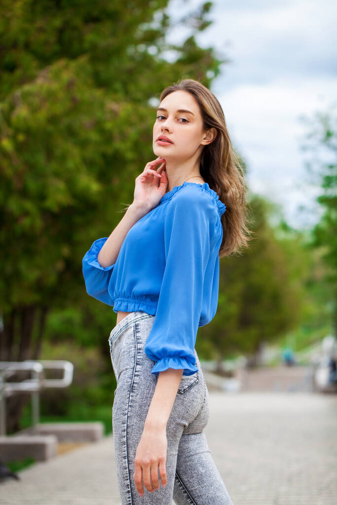 Mladá krásná brunetka dívka v modré blůze a šedé džíny, letní park venkovní  - Fotografie, Obrázek