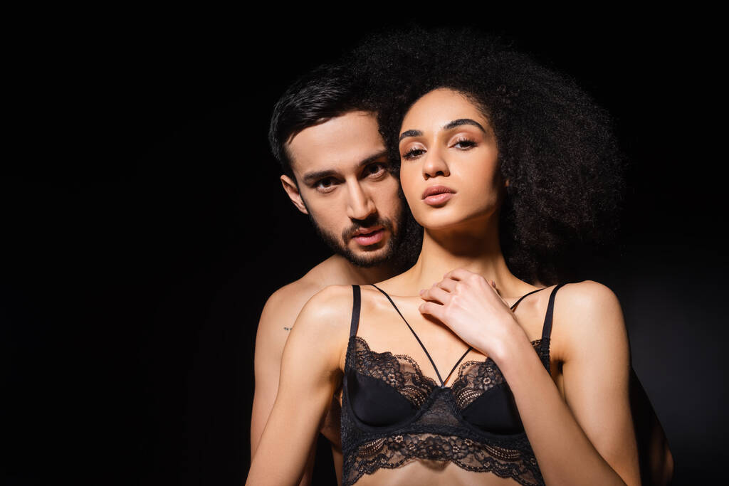Sexy interracial couple looking at camera isolated on black  - Photo, Image