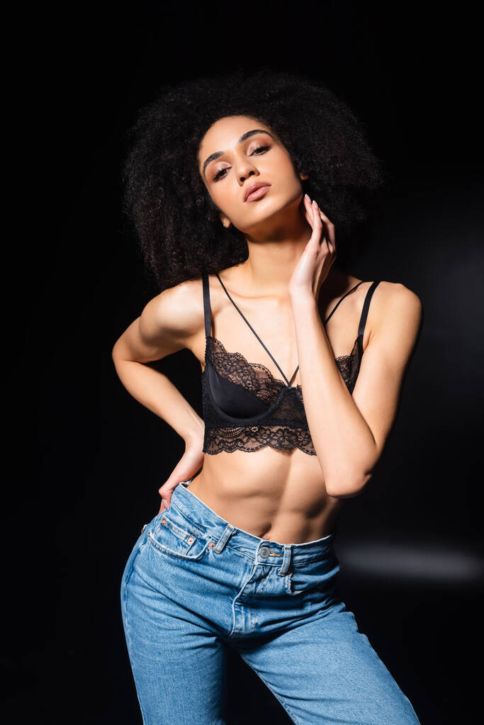 African american woman in lace bra and jeans on black background  - Photo, Image