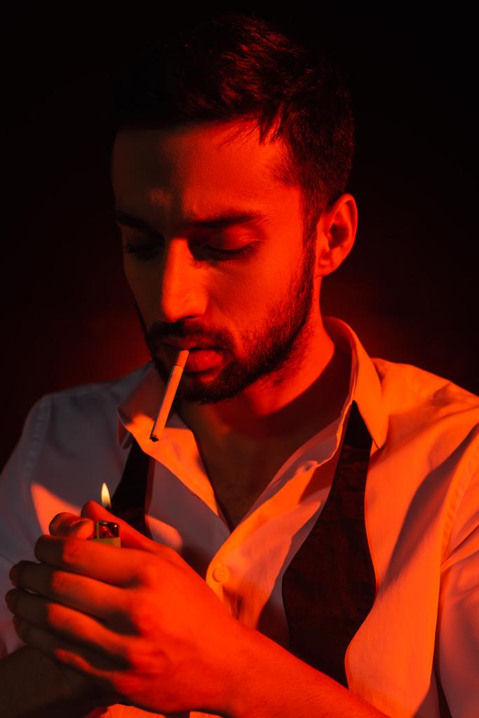 Szakállas férfi cigarettatartó öngyújtó piros fényben fekete háttér  - Fotó, kép