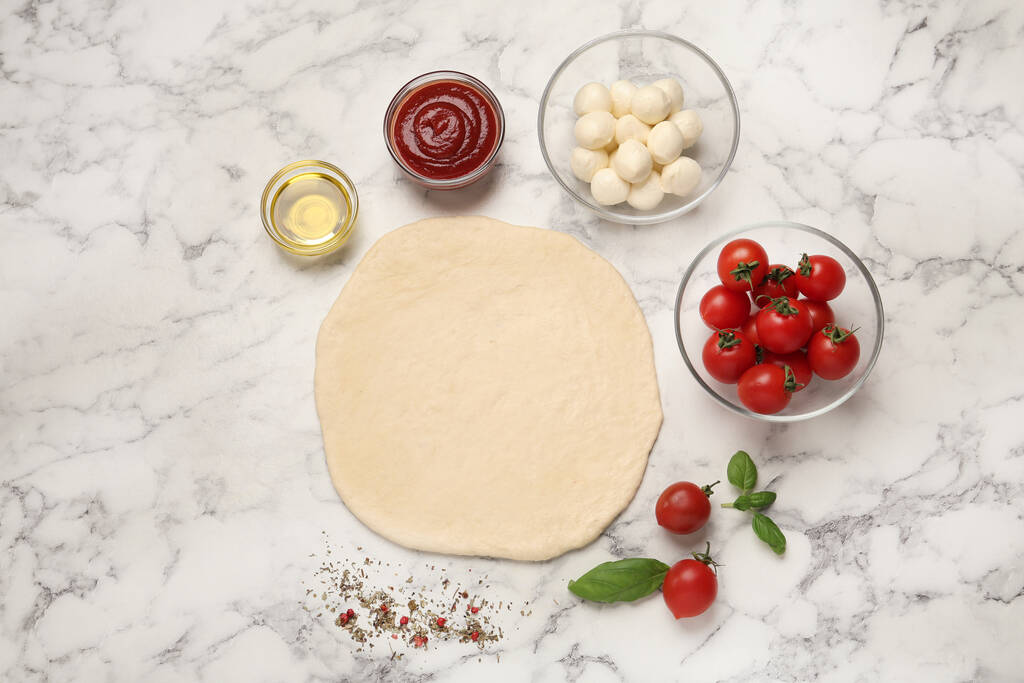 Rauw pizzadeeg en andere ingrediënten op witte marmeren tafel, plat gelegd - Foto, afbeelding