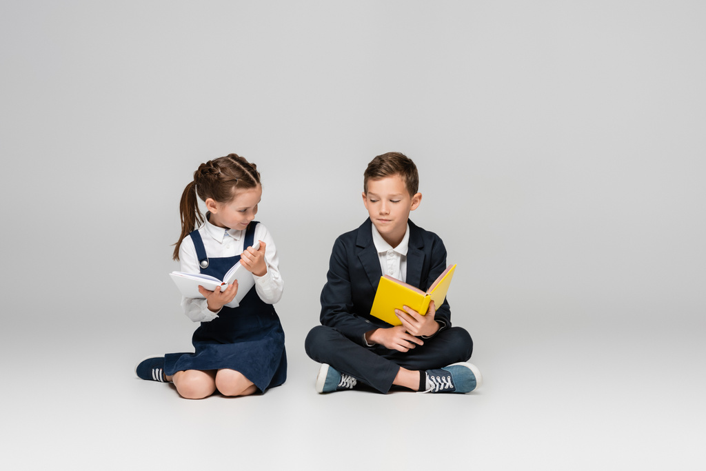 schoolkinderen zitten met boeken en glimlachen op grijs - Foto, afbeelding