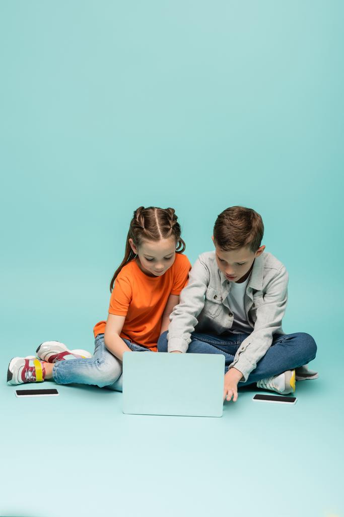 kids using laptop near smartphones with blank screen on blue - Photo, Image