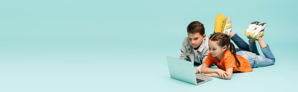 bambini che guardano film sul computer portatile mentre giacciono sul blu, striscione - Foto, immagini