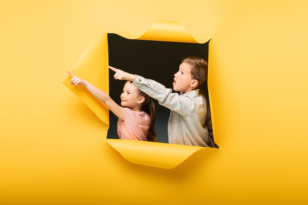Çocuklar sarı arka plandaki delikten parmaklarını göstererek uzaklaşıyor. - Fotoğraf, Görsel
