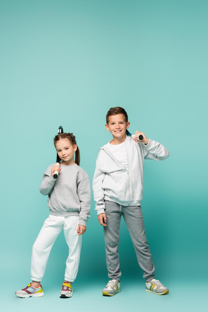 sportowe dzieci w odzieży sportowej stojące z rakietami tenisowymi i uśmiechnięte na niebiesko - Zdjęcie, obraz