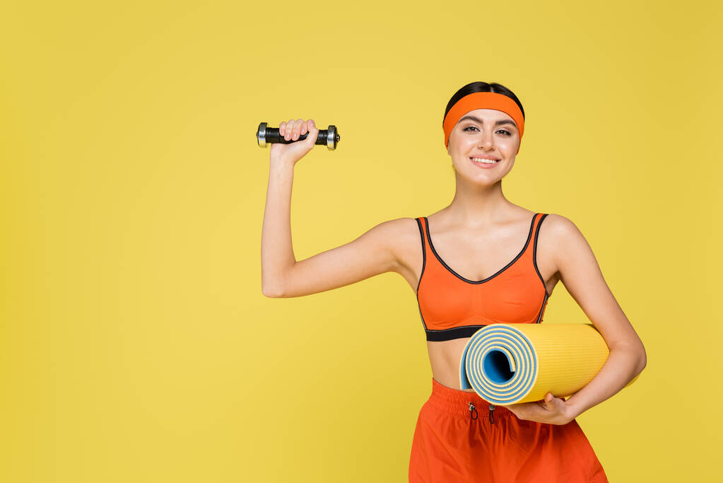 молода спортсменка з фітнес-матом вправи з гантелі ізольовані на жовтому
 - Фото, зображення