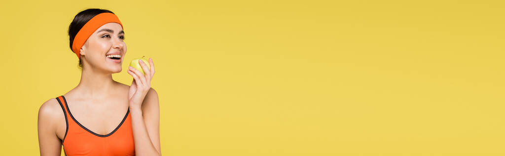 sorrindo esportista com maçã suculenta olhando para longe isolado em amarelo, banner - Foto, Imagem