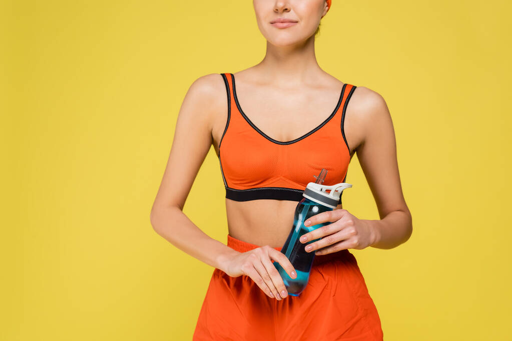 cropped view of woman in orange sportswear holding sports bottle isolated on yellow - Photo, Image