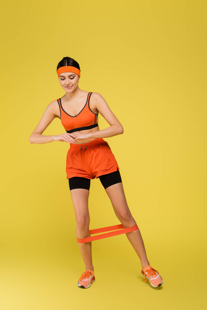 young sportive woman working out with elastics on yellow background - Foto, Imagen