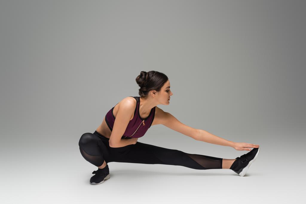 pretty sportswoman stretching on grey background - Photo, Image