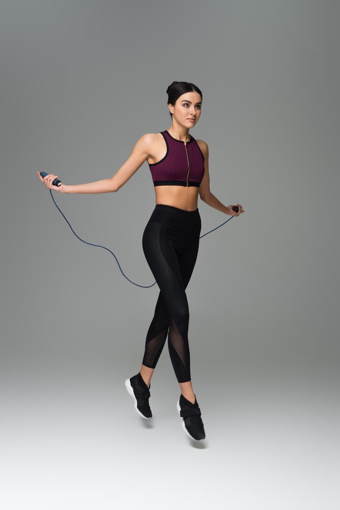 full length view of sportive woman training with jump rope on grey background - Photo, Image