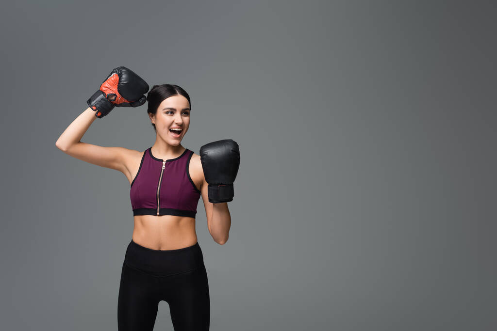 excited sportswoman in boxing gloves showing win gesture isolated on grey - Foto, imagen