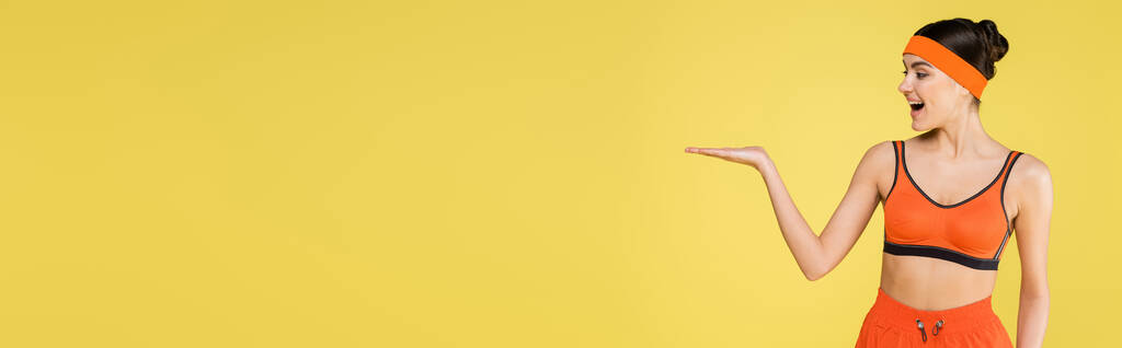 donna sportiva stupita in piedi con palmo aperto isolato sul giallo, striscione - Foto, immagini