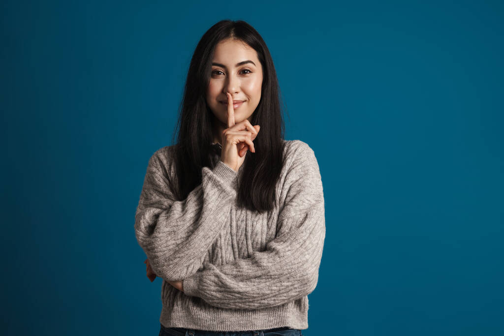 Felice bella ragazza asiatica sorridente e mostrando silenzio gesto isolato su sfondo blu - Foto, immagini