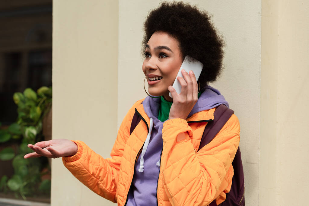 Femme afro-américaine joyeuse parlant sur smartphone près du bâtiment à l'extérieur  - Photo, image