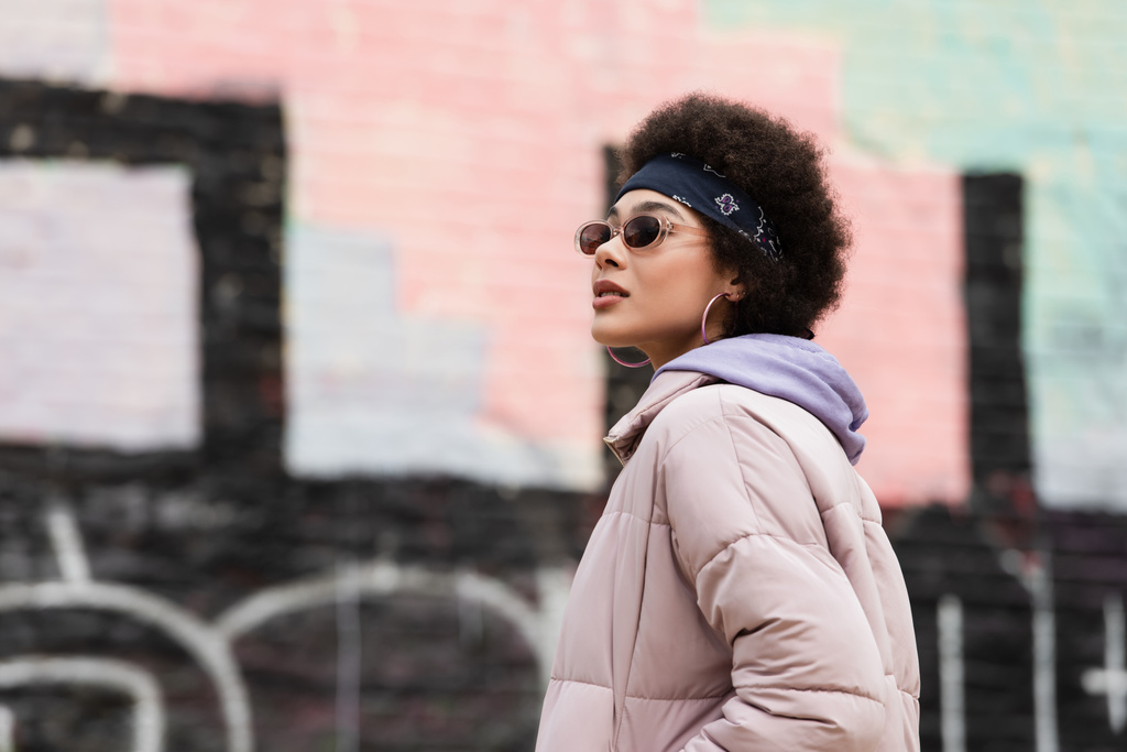 Молодая африканская американка в банданах и солнцезащитных очках стоит на городской улице  - Фото, изображение