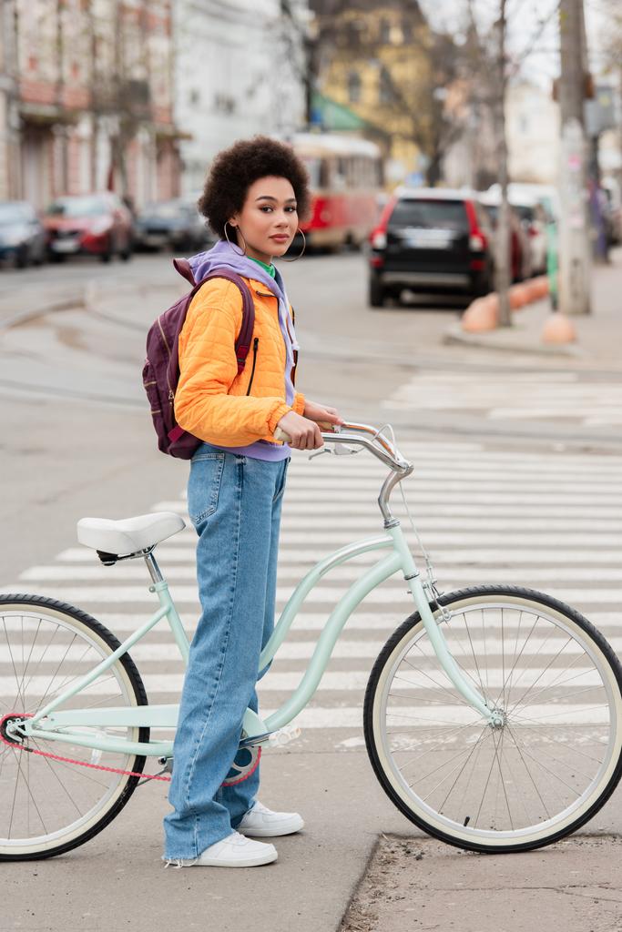 Young african american woman standing near bike on road on urban street  - Photo, Image