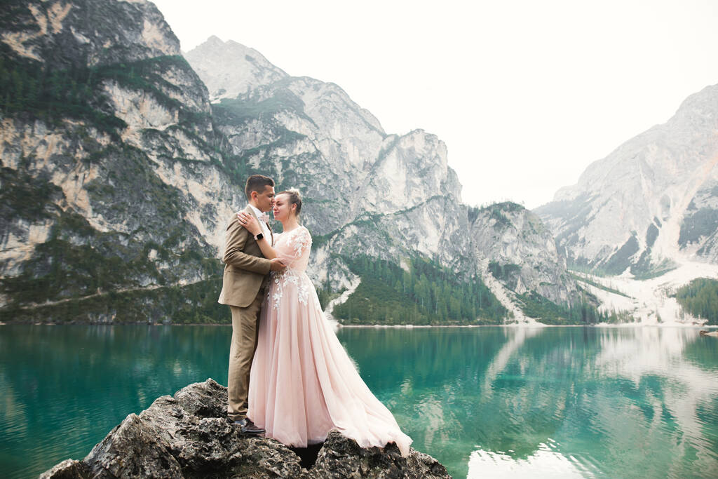 Doğadaki düğün çifti, dağlardaki güzel bir gölün yanında birbirlerine sarılıyorlar beyaz elbiseli güzel model kız. Takım elbiseli adam - Fotoğraf, Görsel