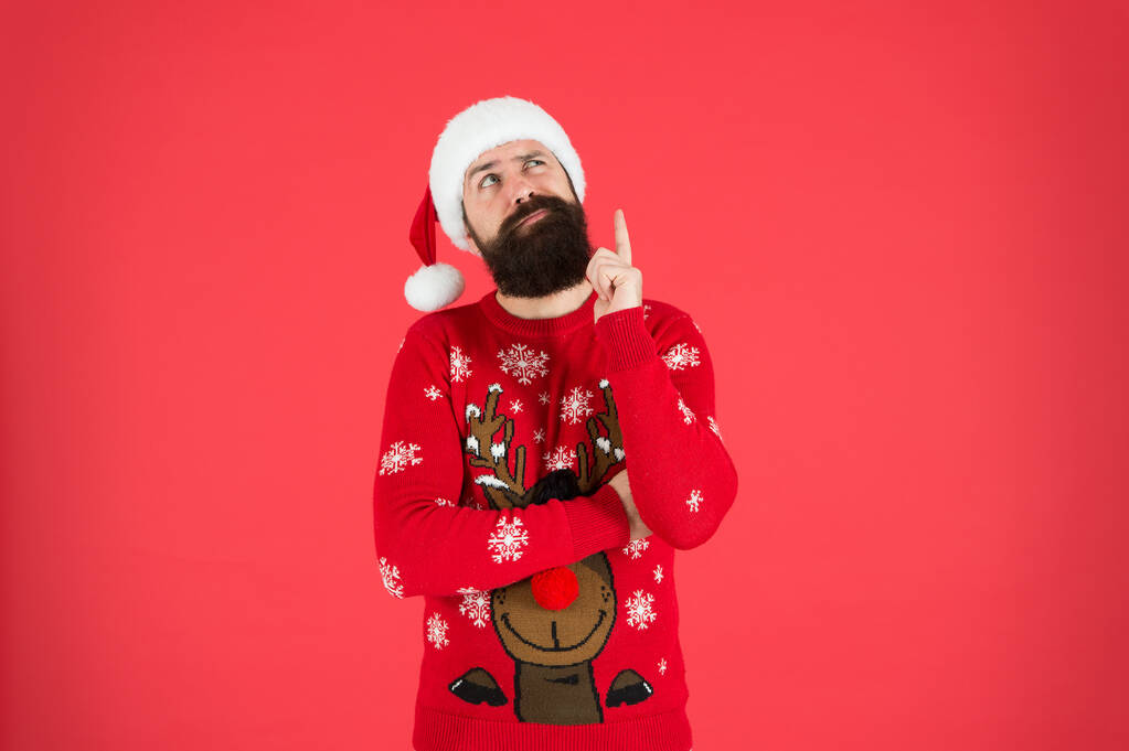 Wintermode. Kerl in Winterkleidung. Bärtiger Weihnachtsmann roter Hintergrund. Irgendetwas in seinem Kopf. Winterurlaub. Männer bärtige Hipster tragen winterliche Strickmützen. Friseur Gesichtsbehaarung - Foto, Bild