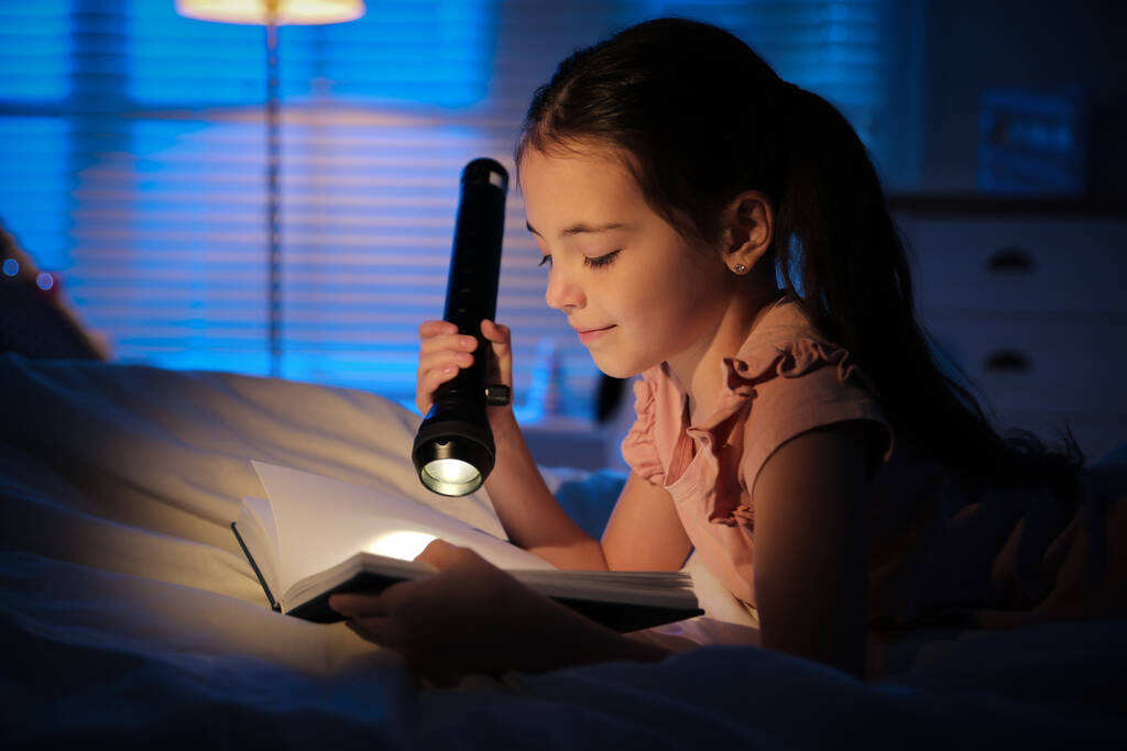 Pieni tyttö taskulamppu käsittelyssä satu pimeässä makuuhuoneessa - Valokuva, kuva