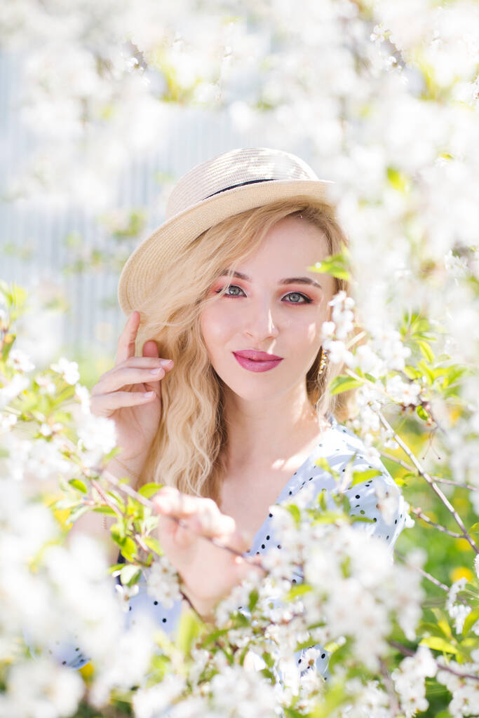  hermosa mujer joven en vestido de verano con sombrero de paja posando en el jardín de primavera en el día soleado - Foto, Imagen