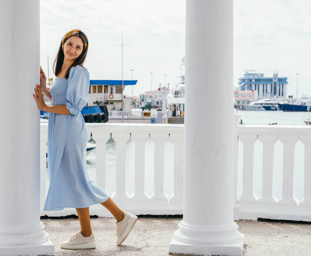 Portret van jonge mooie vrouw in blauwe jurk aan de kust tegen de achtergrond van jachten. Zomer vrouwelijke mode look. - Foto, afbeelding