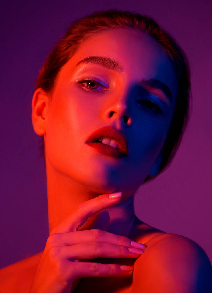 Όμορφη νεαρή γυναίκα με καθαρό τέλειο δέρμα σε μπλε νέον και ροζ φωτιστικό στούντιο. Πορτρέτο του μοντέλου ομορφιάς με φυσικό γυμνό μακιγιάζ και μακριές βλεφαρίδες. - Φωτογραφία, εικόνα