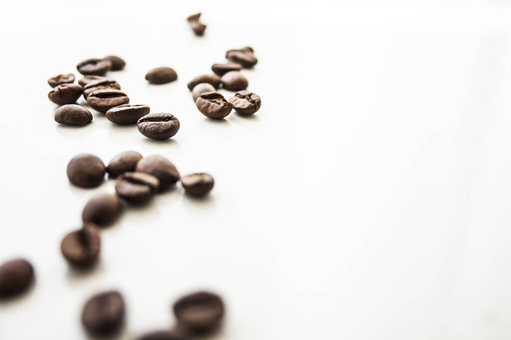A closeup of the roasted coffee beans scattered on the white surface - space for text - Photo, Image