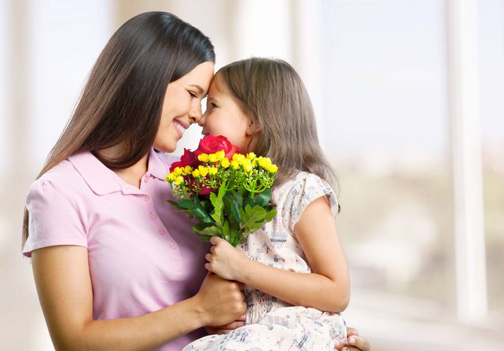 Ragazzo allegro che abbraccia la donna seduta sul divano con bouquet il giorno della mamma - Foto, immagini