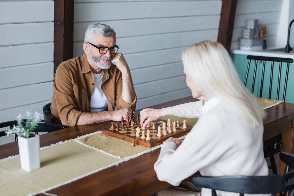 Ανώτερος άνθρωπος που παίζει σκάκι με θολή γυναίκα στο σπίτι - Φωτογραφία, εικόνα