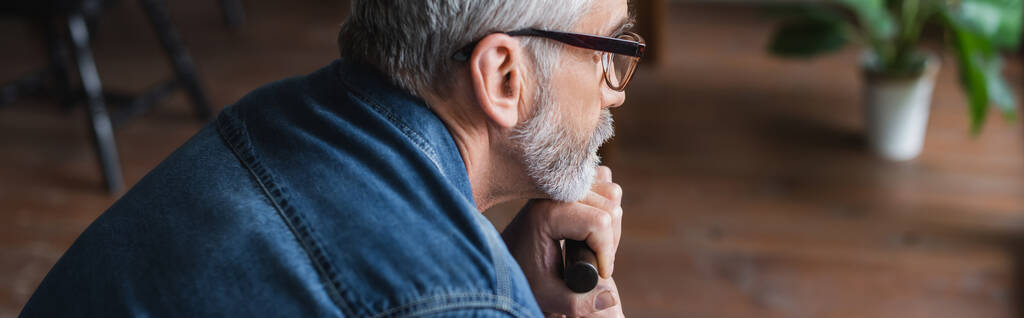 Πλευρική άποψη του ηλικιωμένου άνδρα που κρατά δεκανίκι στο σπίτι, πανό  - Φωτογραφία, εικόνα
